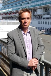1_Cherbourg Tourisme Director Guillaume Hamel stands beside the massive Ventura Cruise Ship at the Cherbourg Cruise Terminal